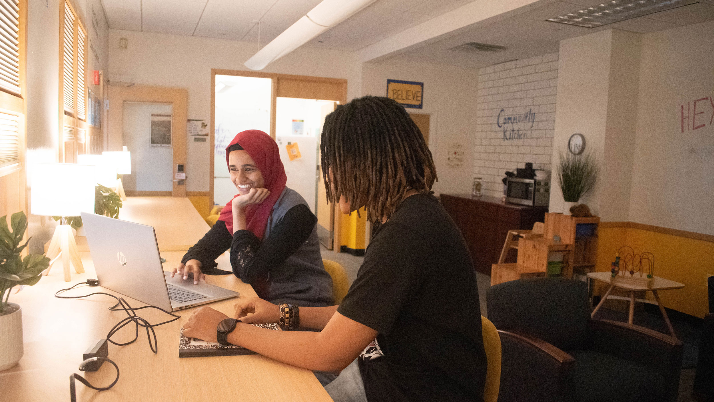 two students sit at high countertop in the student resource center studying on a laptop