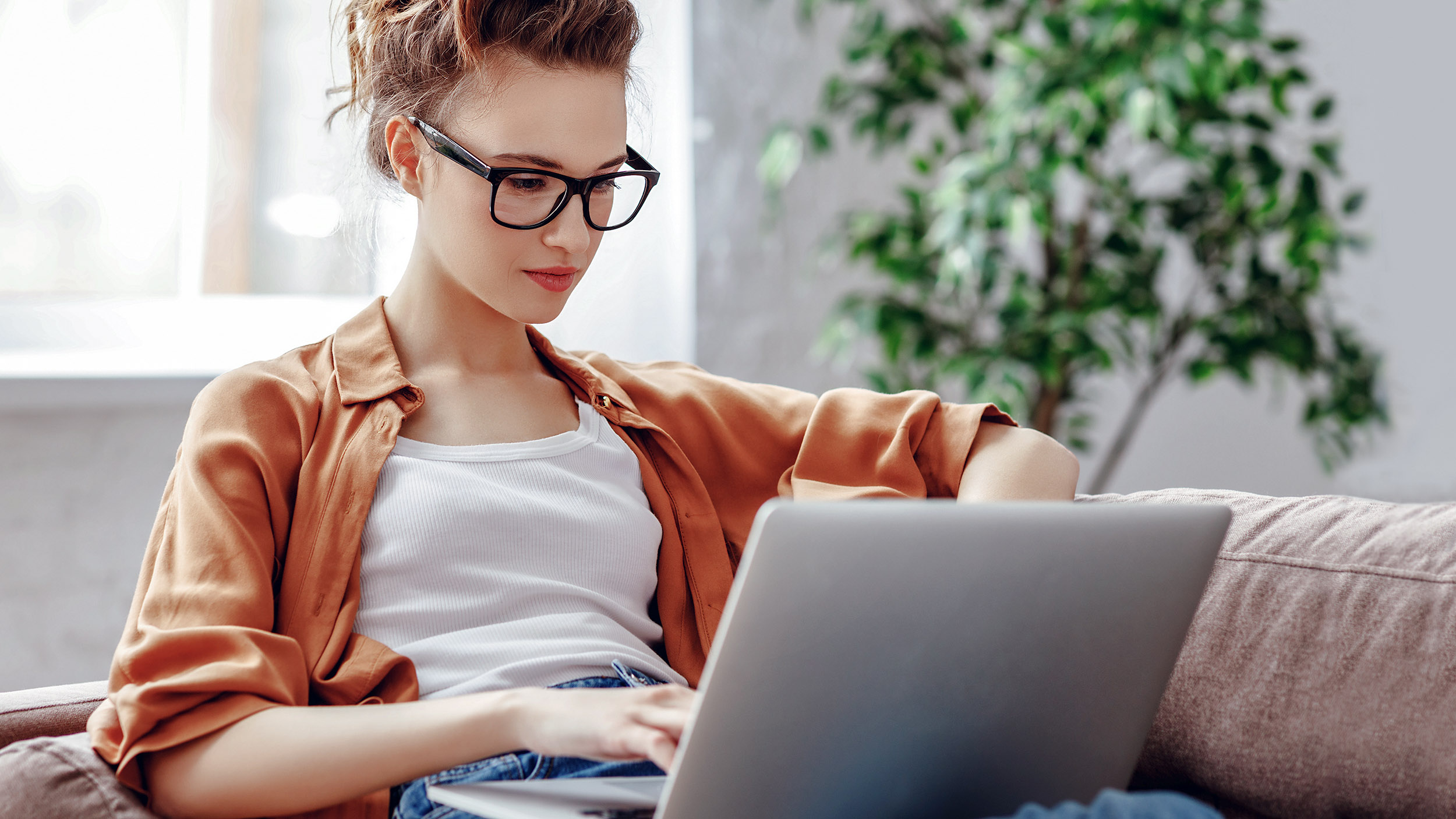 young woman sits on her sofa looking at something on a laptop