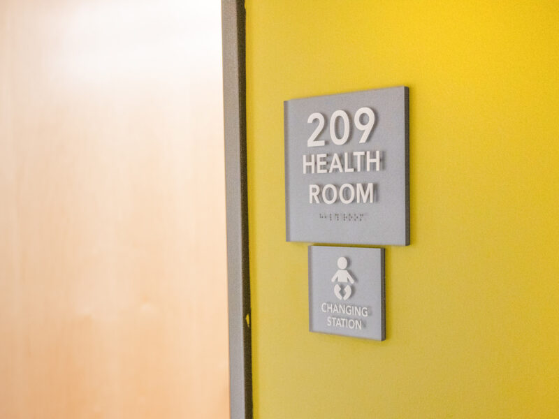 a yellow wall with a health room sign reading room 209 and a baby changing station