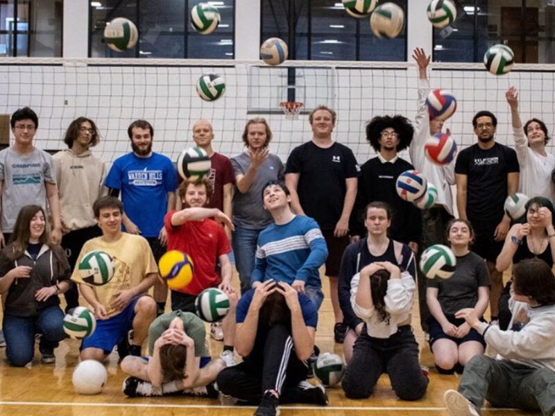 champlain's volleyball club posing for a group photo and throwing volleyballs in the air