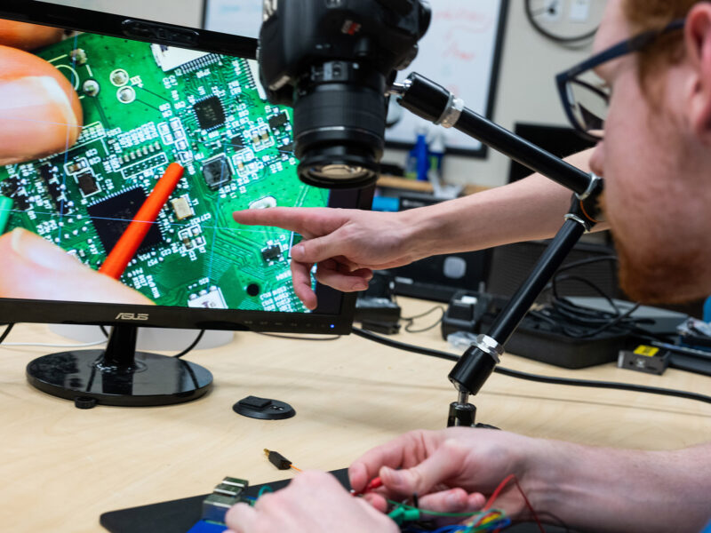 student works on computer hardware, a camera magnifies the work on a computer screen for easier work