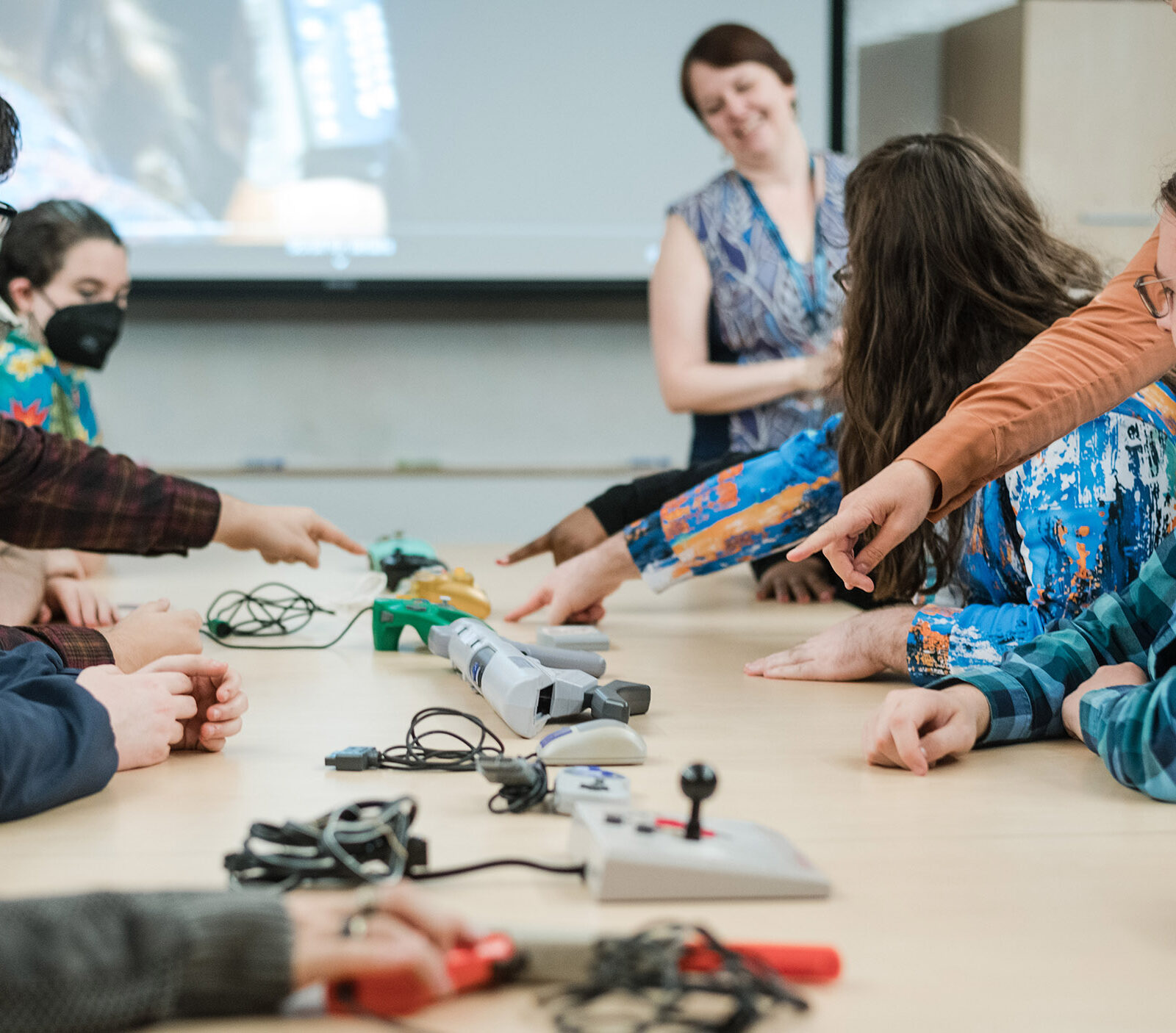 students gathered around a large table where game controllers make a line down the center of the table