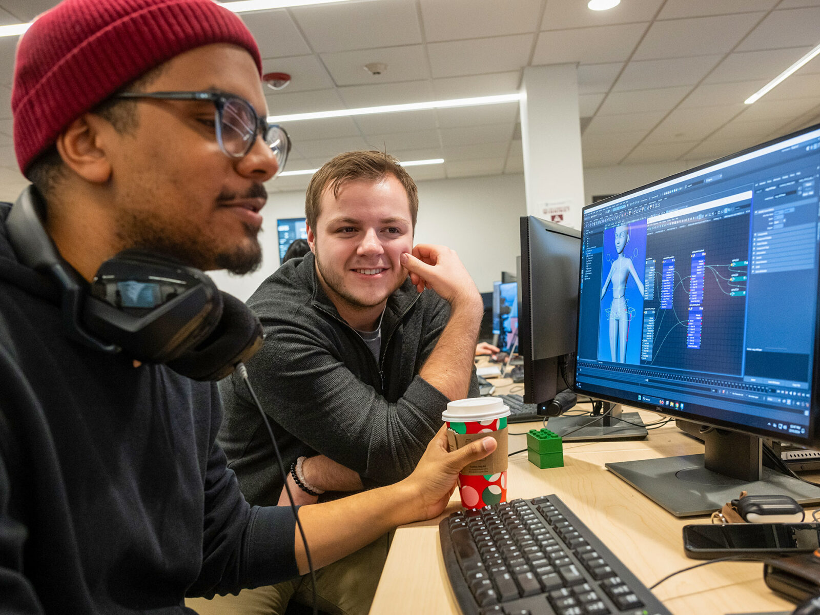 two students working on digital animation in a classroom with a cup of coffee