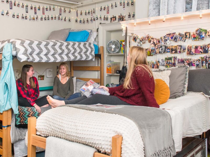 Students hanging out in a decorated dorm room. Photos and lights hang around the room