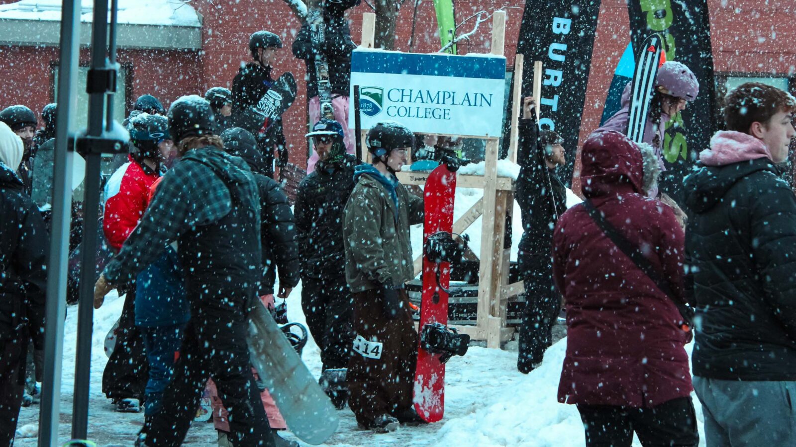 Students standing in the snow near a Champlain College sign holding snowboards