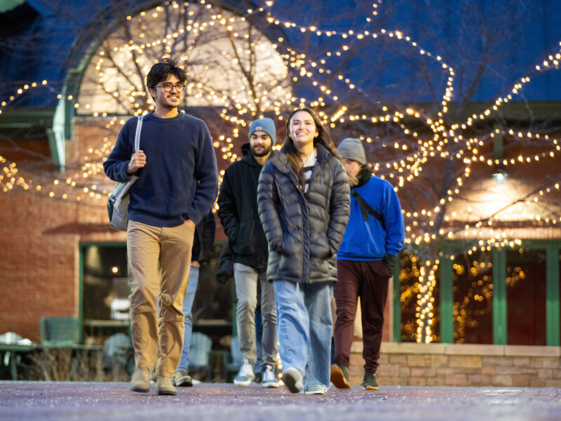 Students walking on campus under Christmas lights in the winter