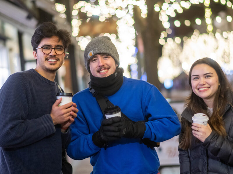 Students posing for a photo holding cups of coffee, smiling on Church Street
