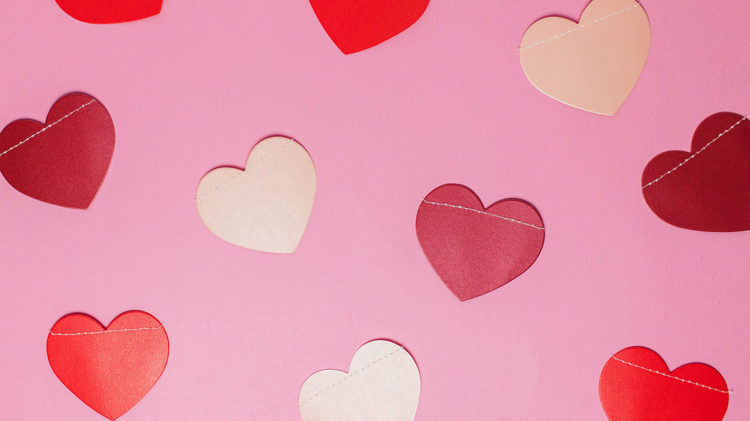 A pink background with different colored paper hearts across the screen