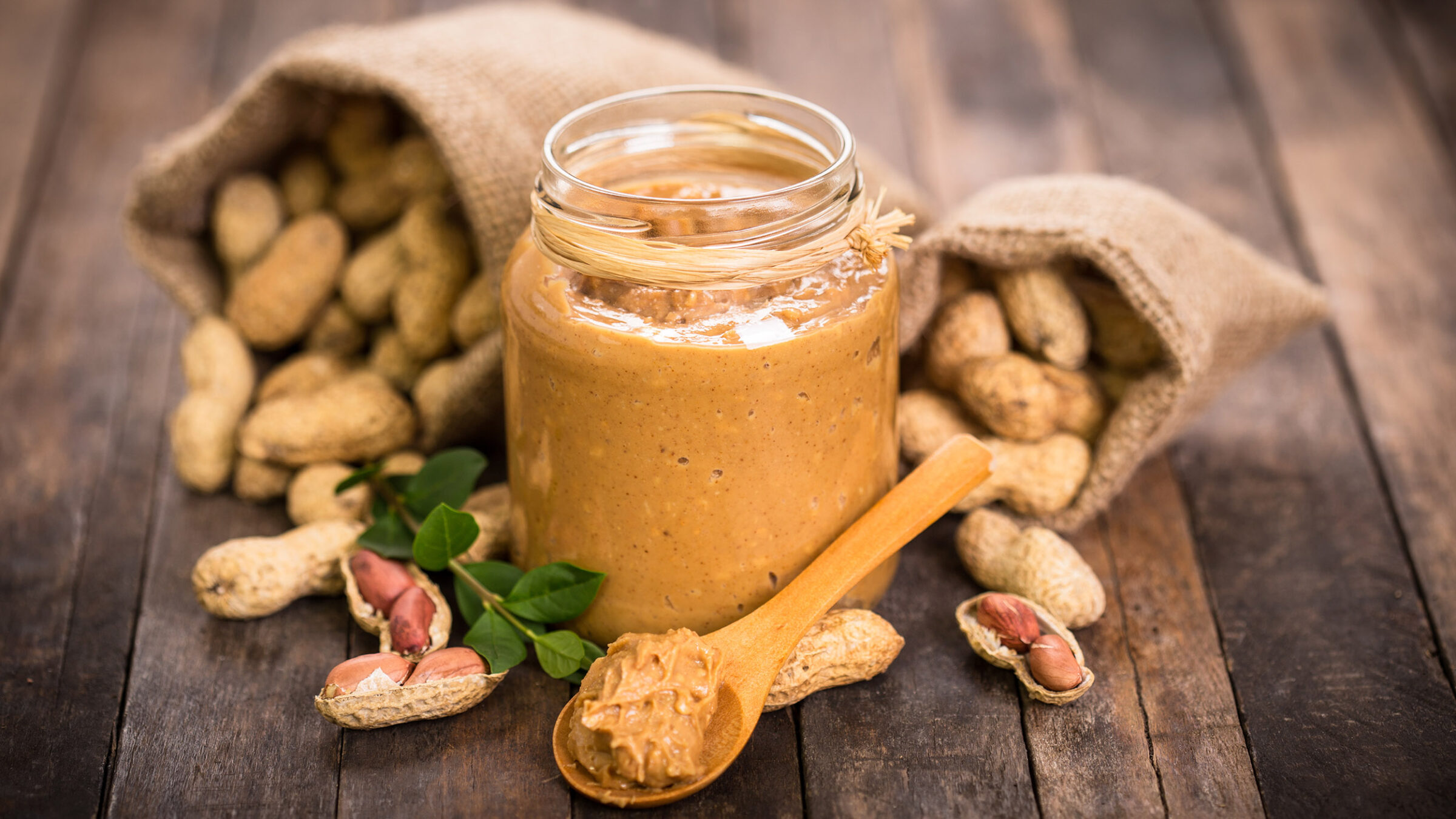 Spoon and glass jar with creamy peanut butter on kitchen table, closeup