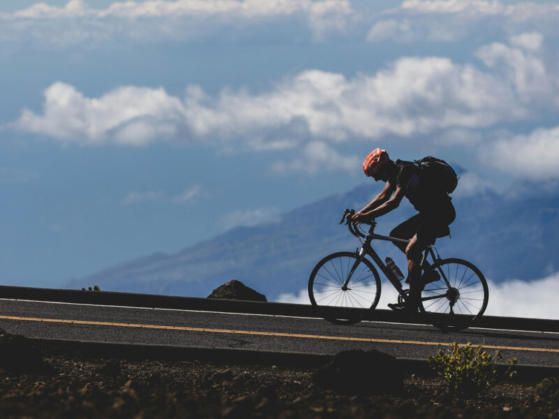 person biking on a road with mountains in the background and blue sky