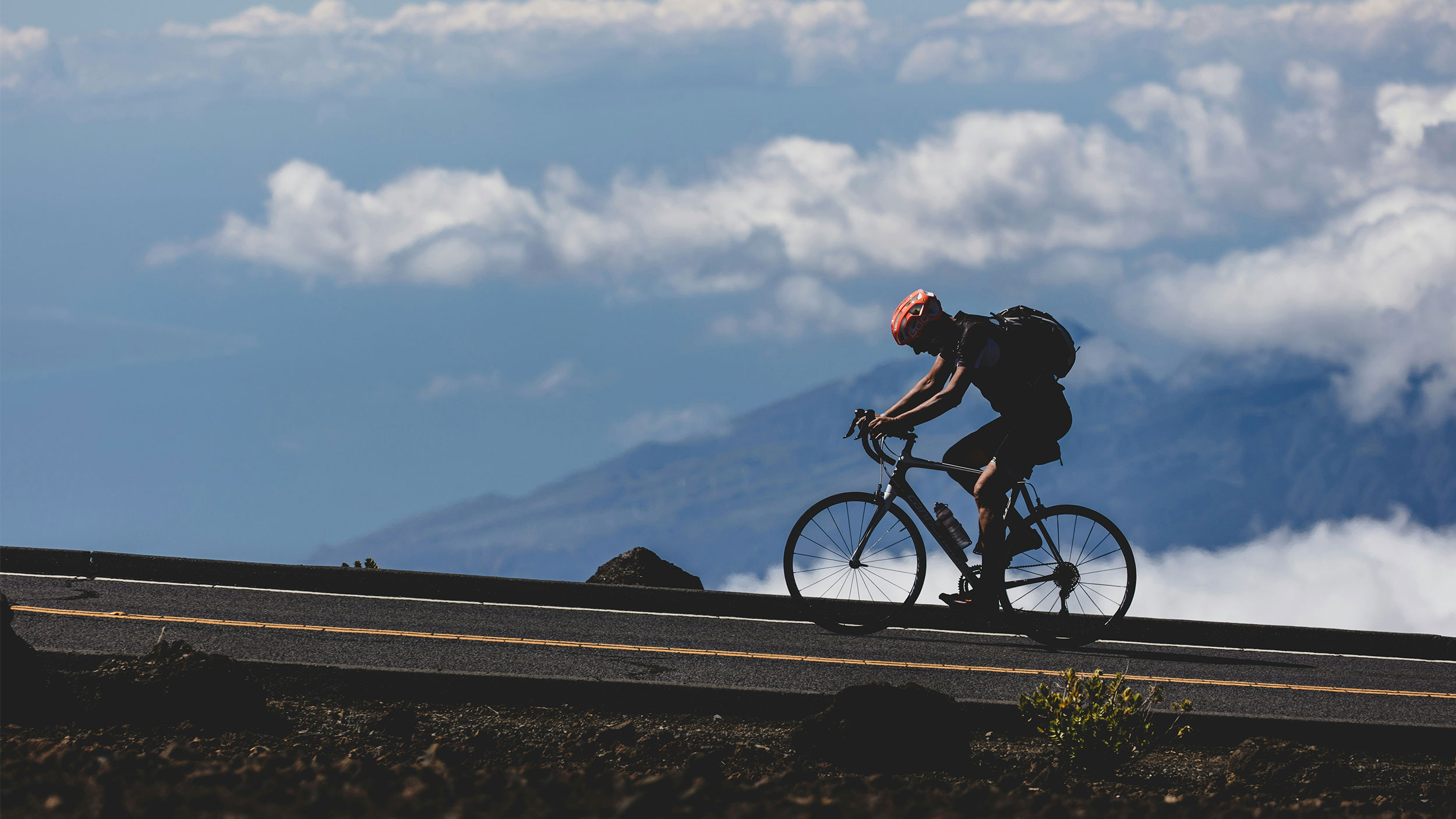 person biking on a road with mountains in the background and blue sky
