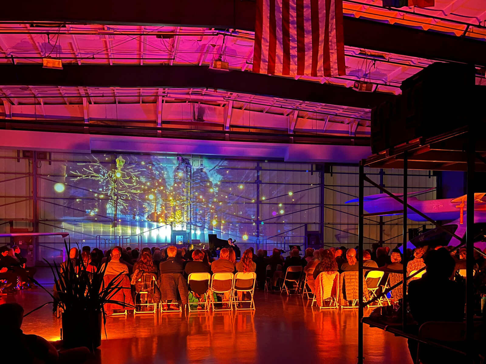Projection art on display inside an airplane hangar, accompanied by an orchestra.