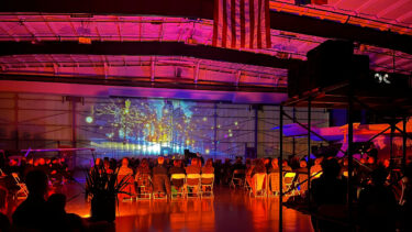 Projection art on display inside an airplane hangar, accompanied by an orchestra.