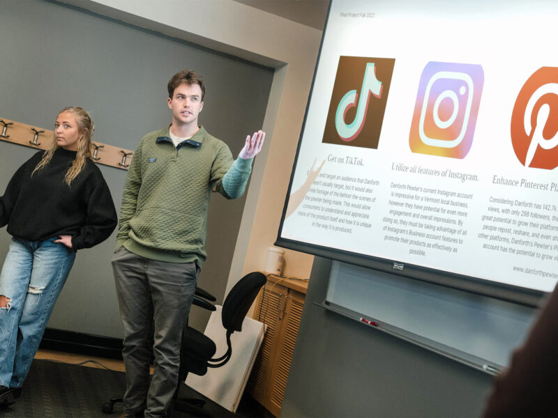 two students present their work to the class via a slide presentation