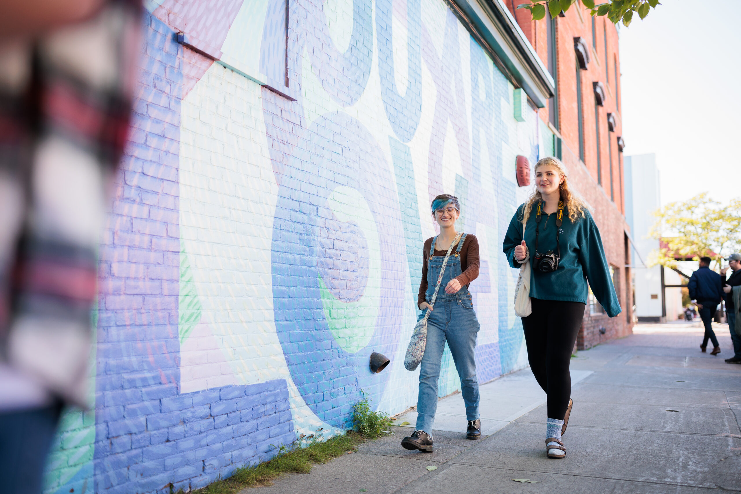 two students talk by an outdoor wall that says "you are loved"