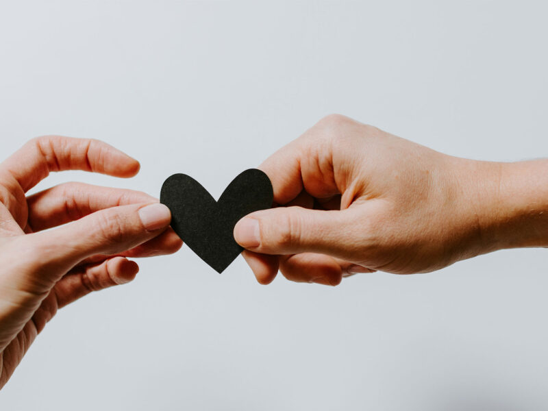 two hands hold a black paper heart