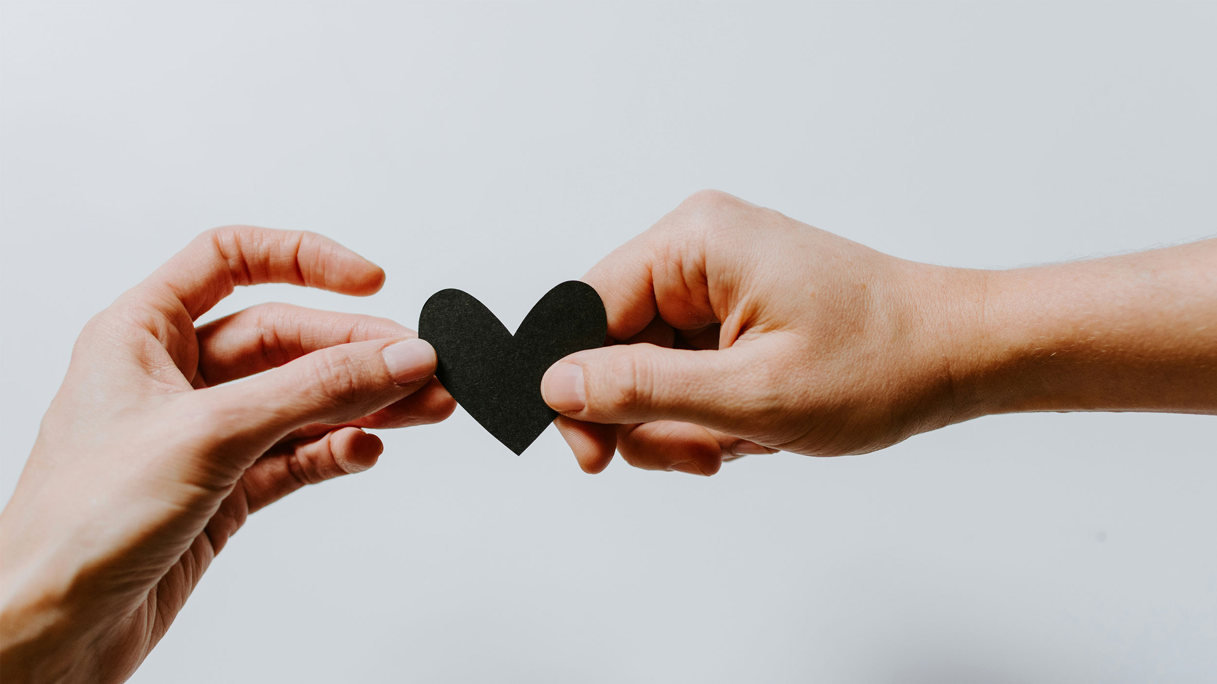 two hands hold a black paper heart