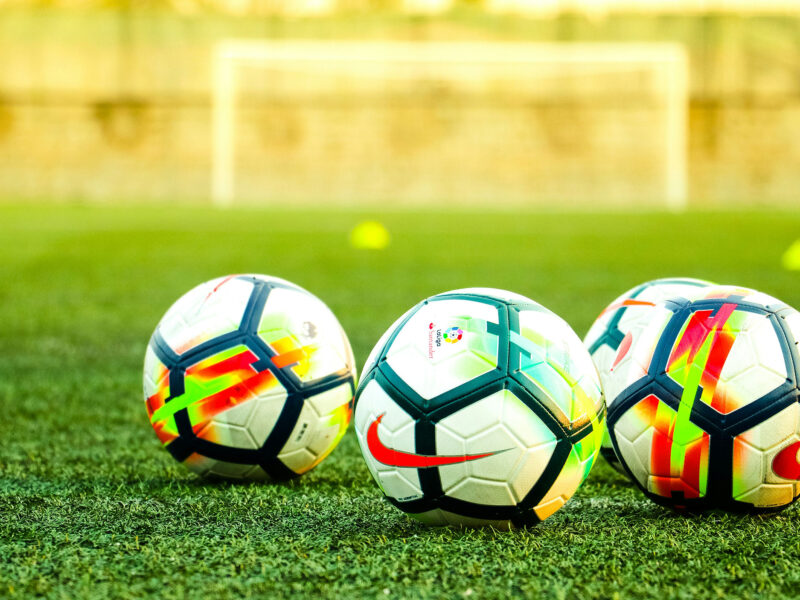 three soccer balls on a grassy soccer field