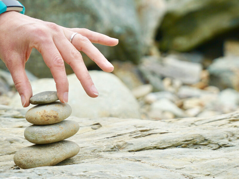 a hand touches a small tower of 4 rocks