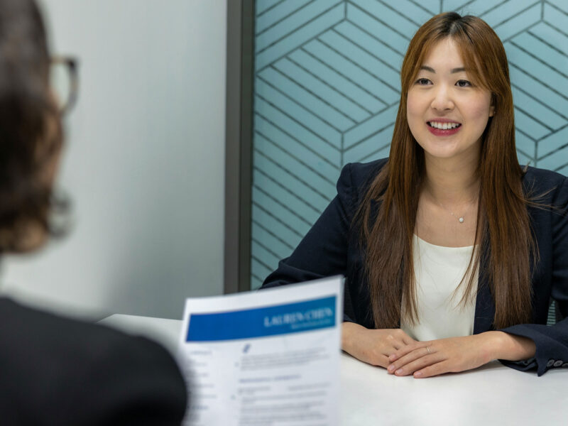 person smiles sitting at a table, sitting across from a person who is reading their resume