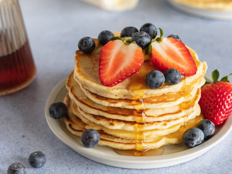 A stack of pancakes on a table with fruit