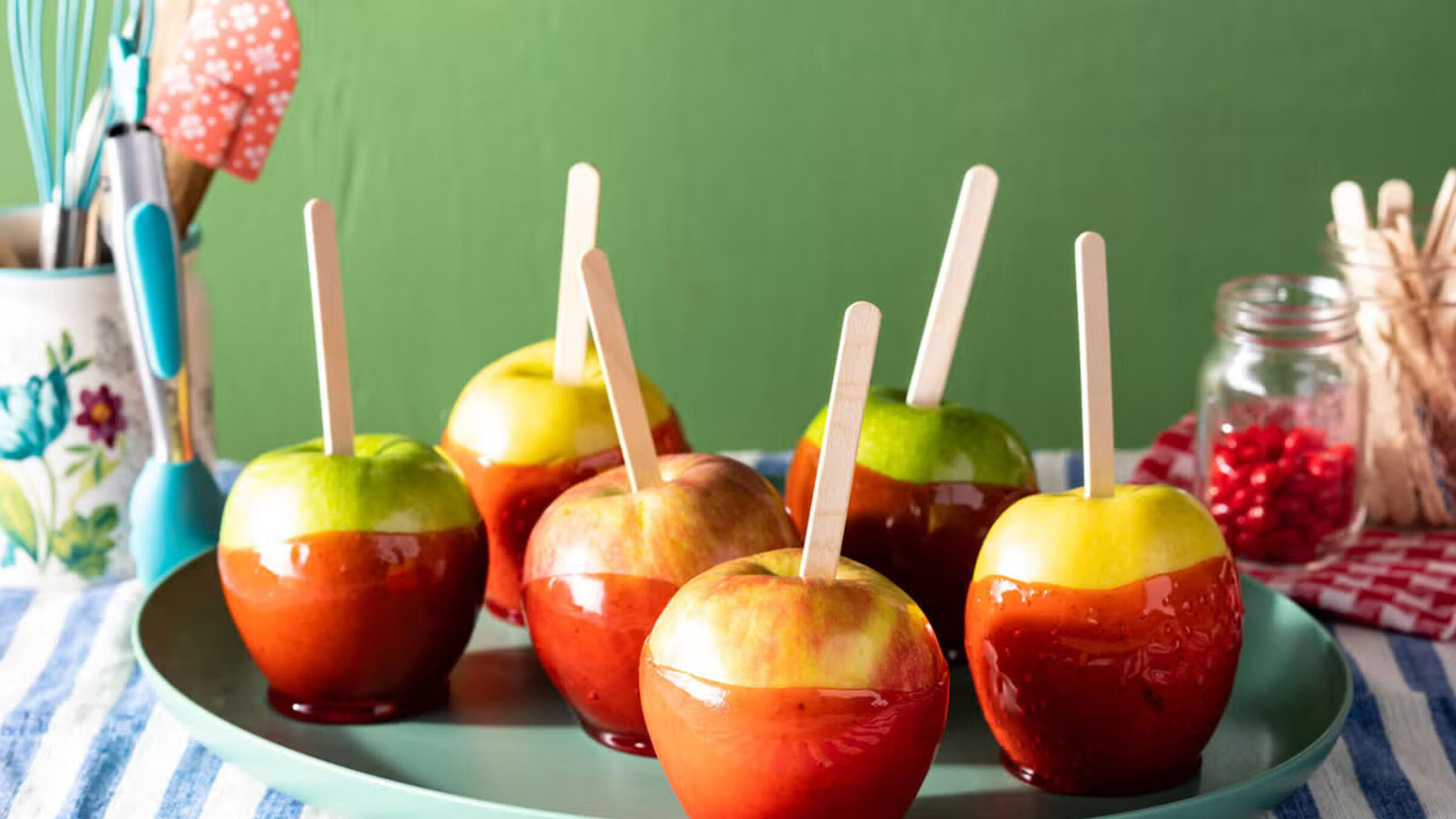 A stock photo of candy apples on a tray in front of a green background