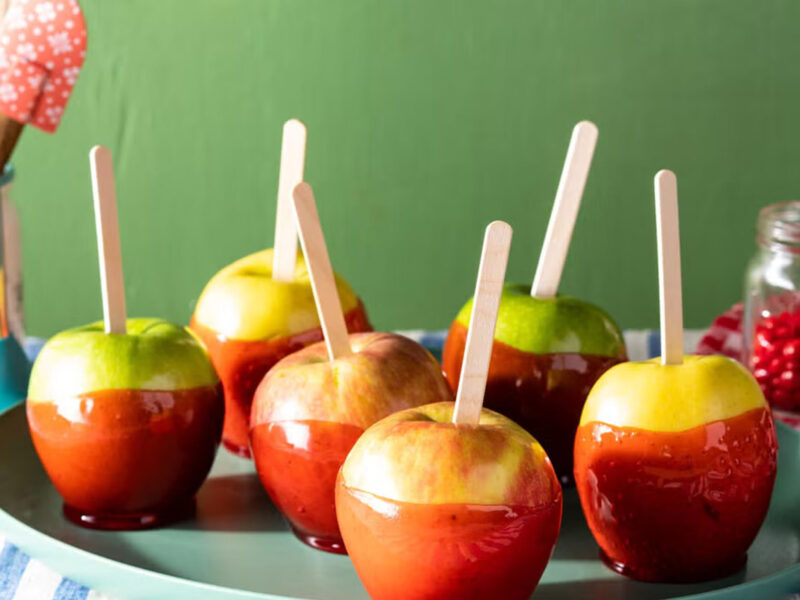 A stock photo of candy apples on a tray in front of a green background