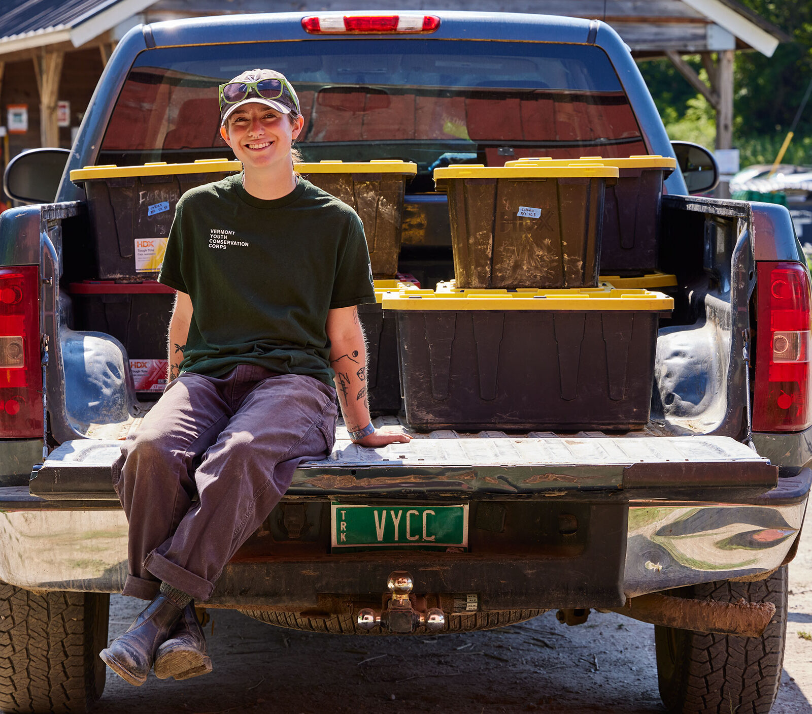 Morgan Chesnais sits on the bed of a pickup truck at their internship at an 11-acre farm owned by VYCC.