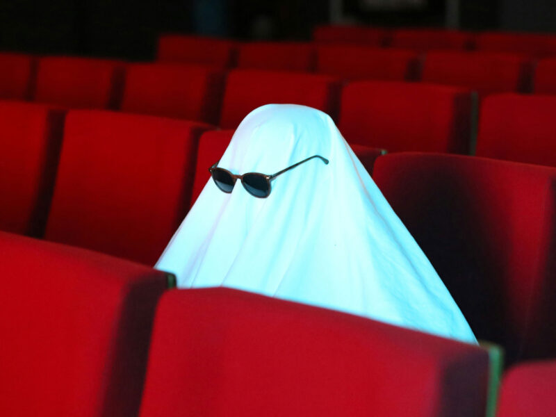 ghost with sunglasses sitting in red movie theatre seats