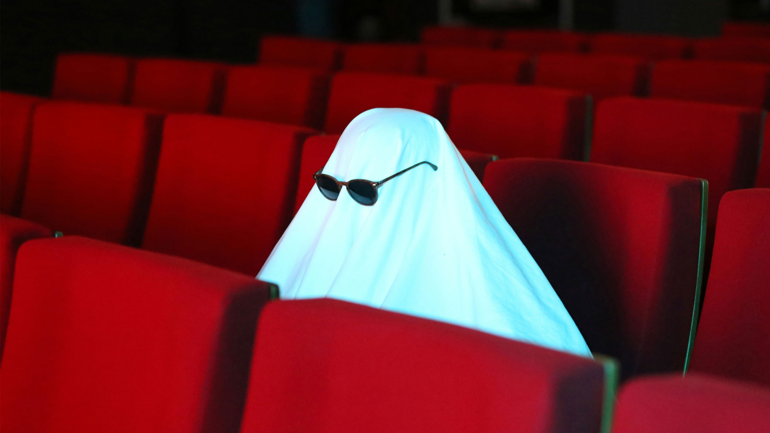 ghost with sunglasses sitting in red movie theatre seats
