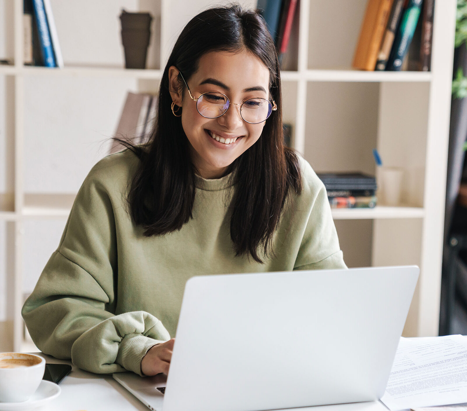 student smiling looking at laptop in modern office with a cup of coffee next to them