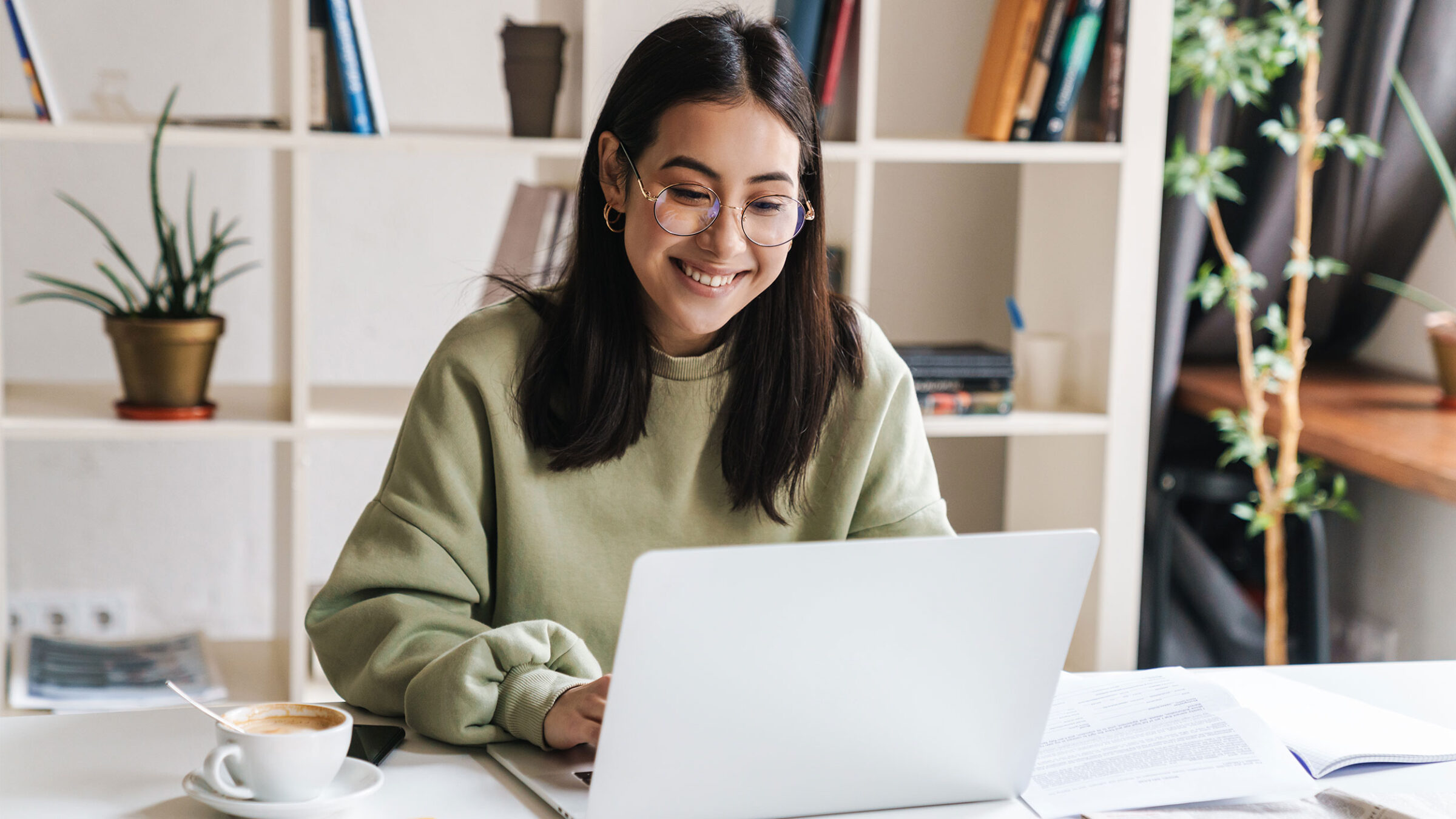 student smiling looking at laptop in modern office with a cup of coffee next to them