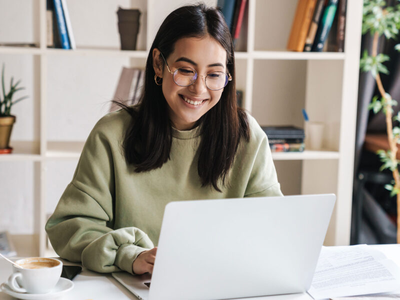 student smiling looking at laptop in modern office with a cup of coffee next to them