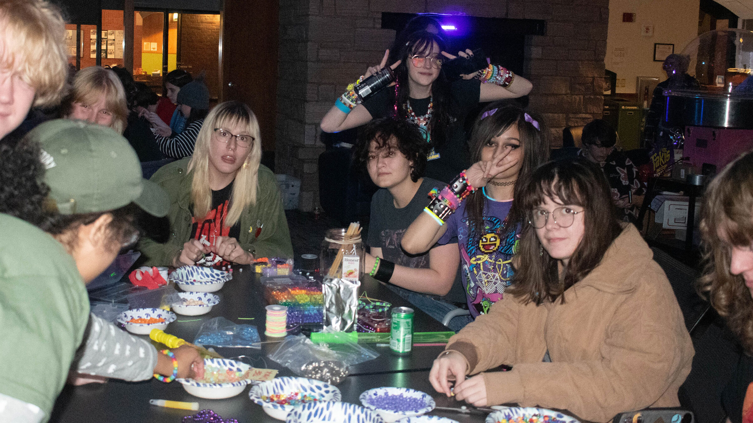 students sit at table making colorful beaded bracelets
