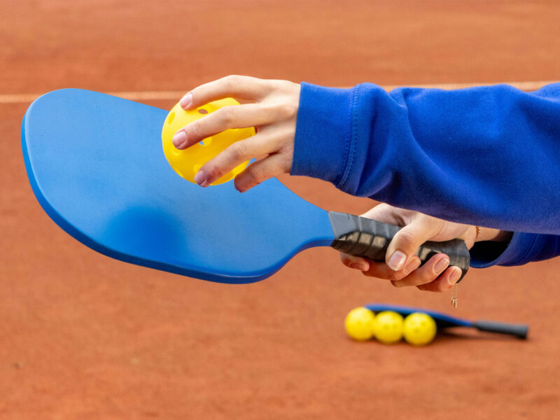 hand holding a pickleball racket and ball