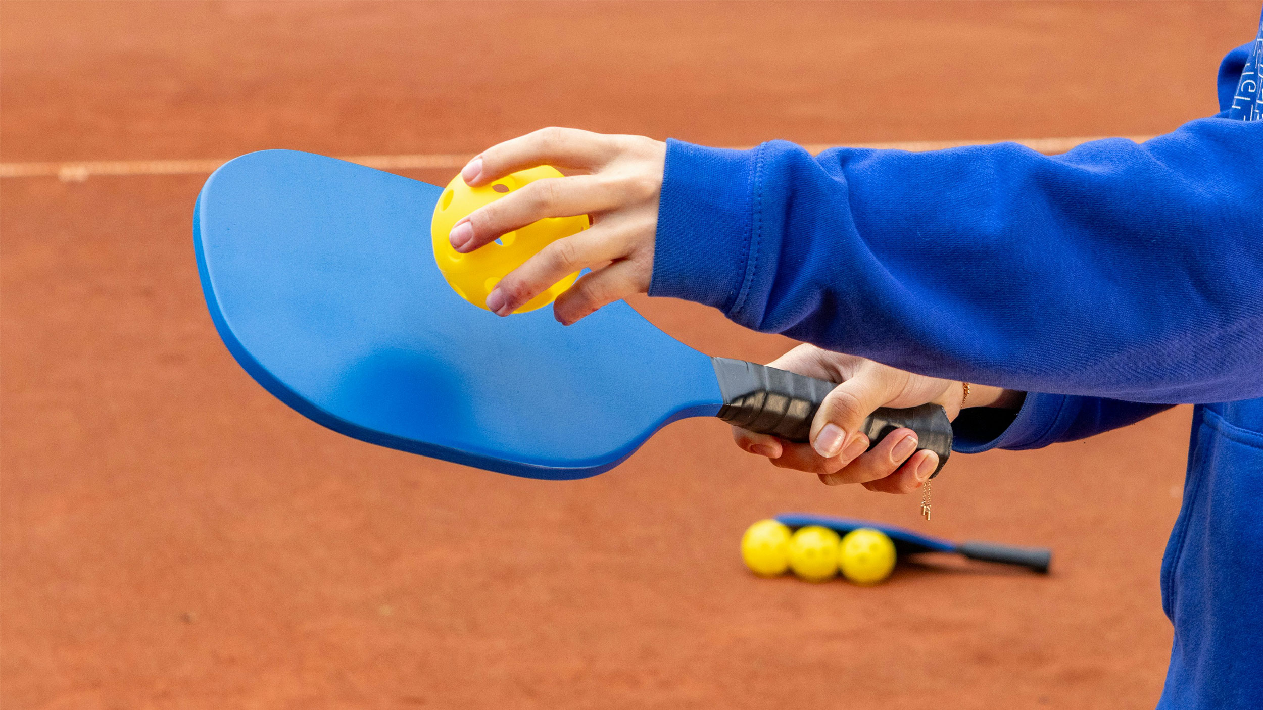 hand holding a pickleball racket and ball