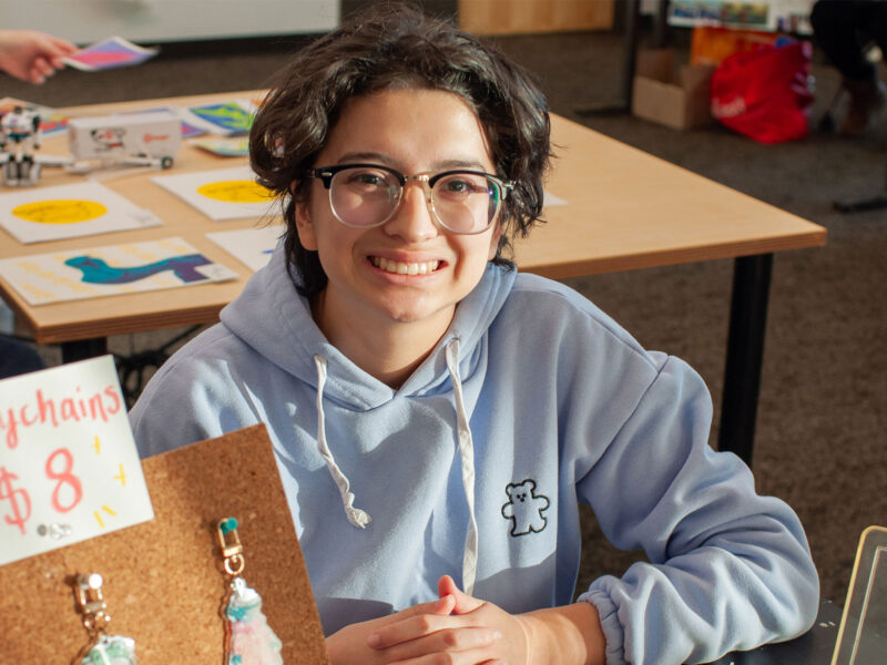 student smiling while sitting at a table selling their homemade keychains