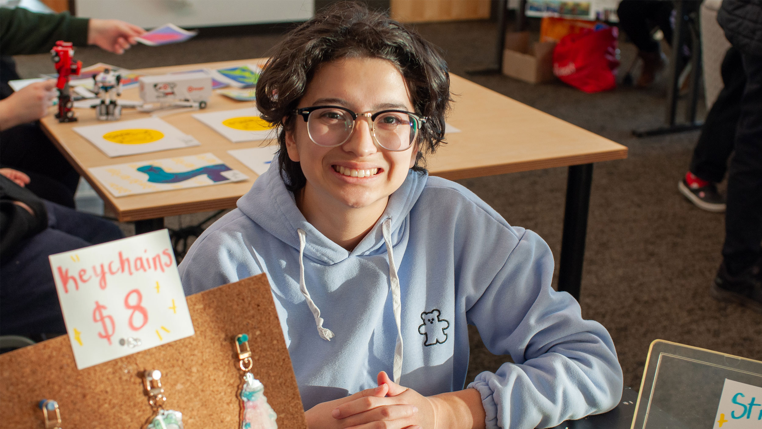 student smiling while sitting at a table selling their homemade keychains