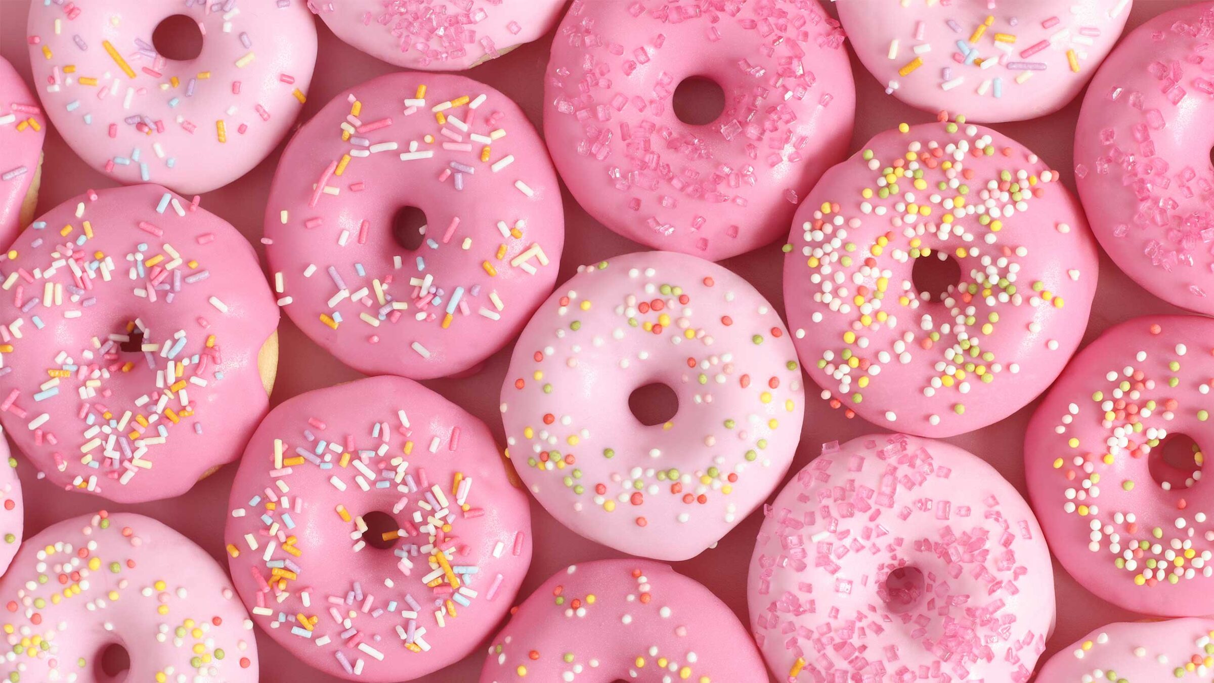 pink donuts with rainbow sprinkles against a pink backgorund