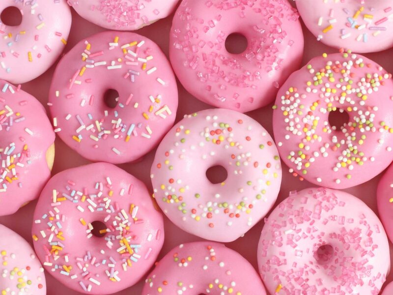 pink donuts with rainbow sprinkles against a pink backgorund