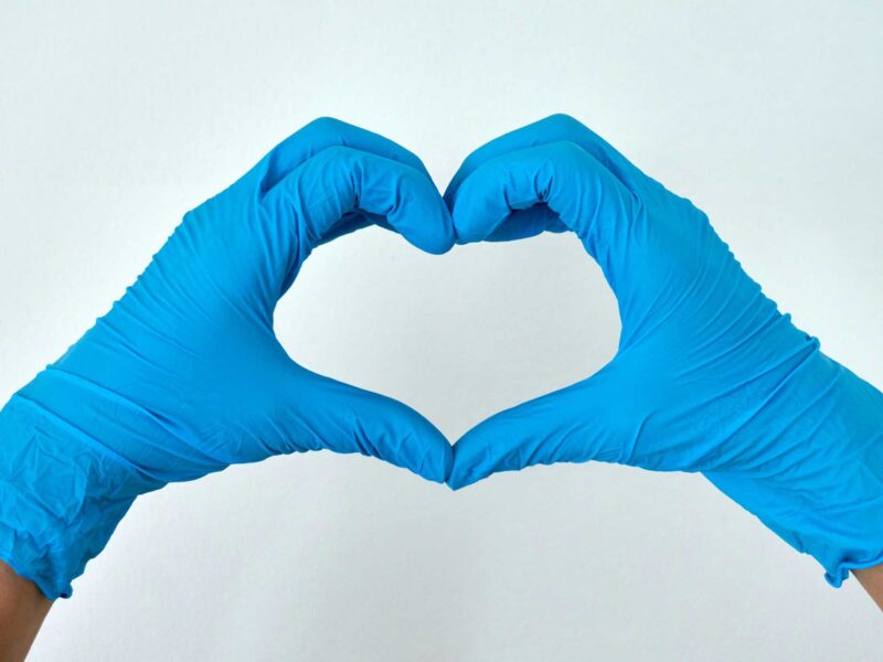 a person makes a heart with their hands while wearing blue surgical gloves