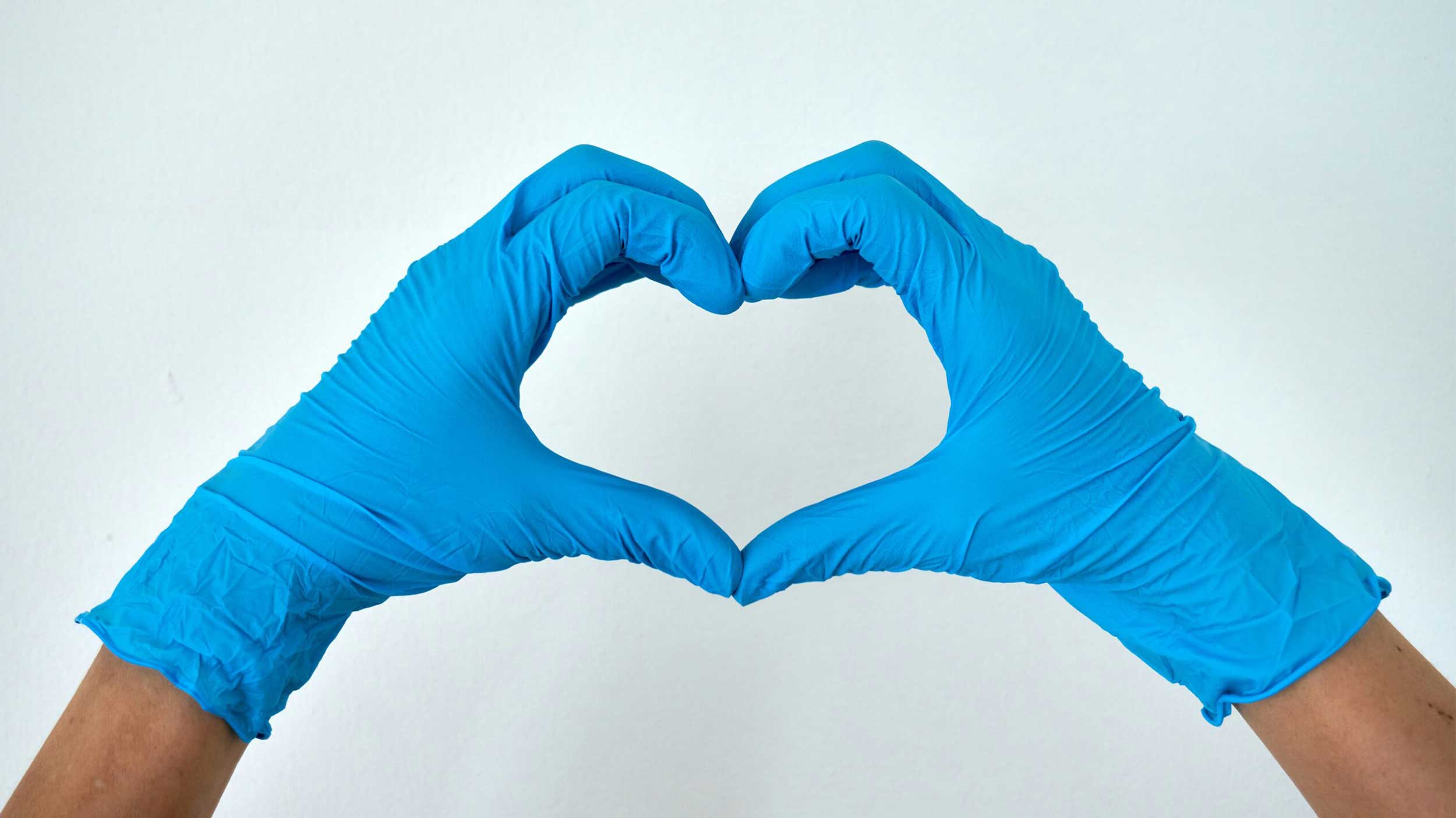a person makes a heart with their hands while wearing blue surgical gloves