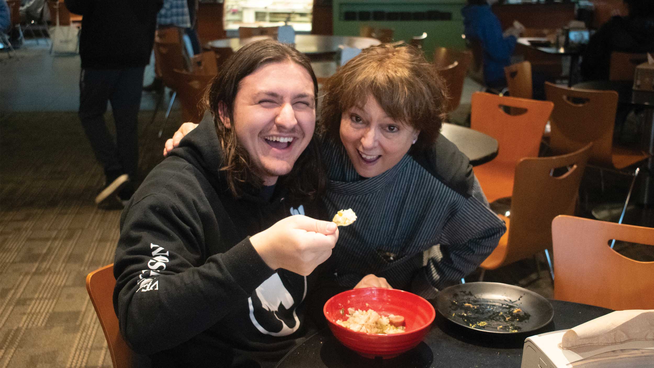 two individuals smiling with a bowl of food
