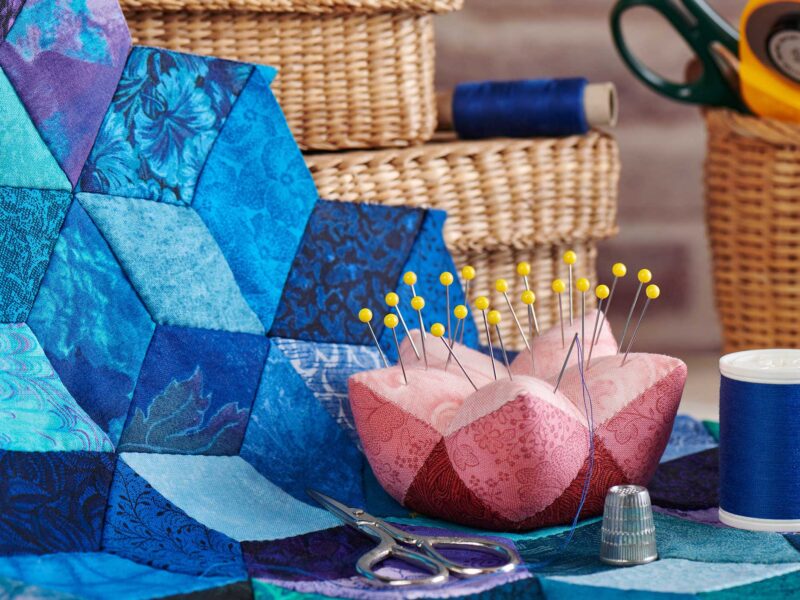 pink pin cushion and other quilting supplies on top of a blue and purple quilt