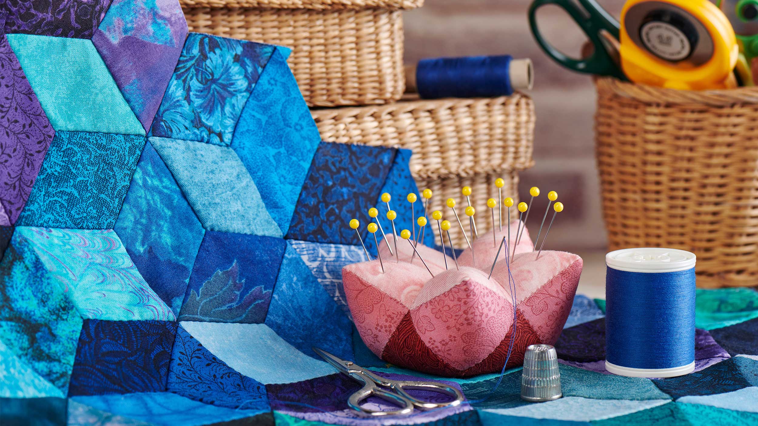 pink pin cushion and other quilting supplies on top of a blue and purple quilt