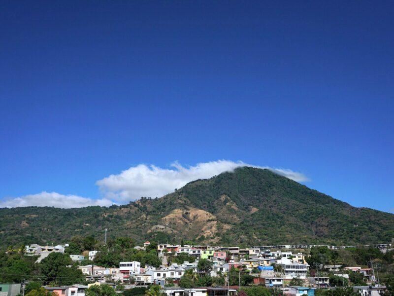 A landscape with housing and a mountain against a blue sky with some clouds