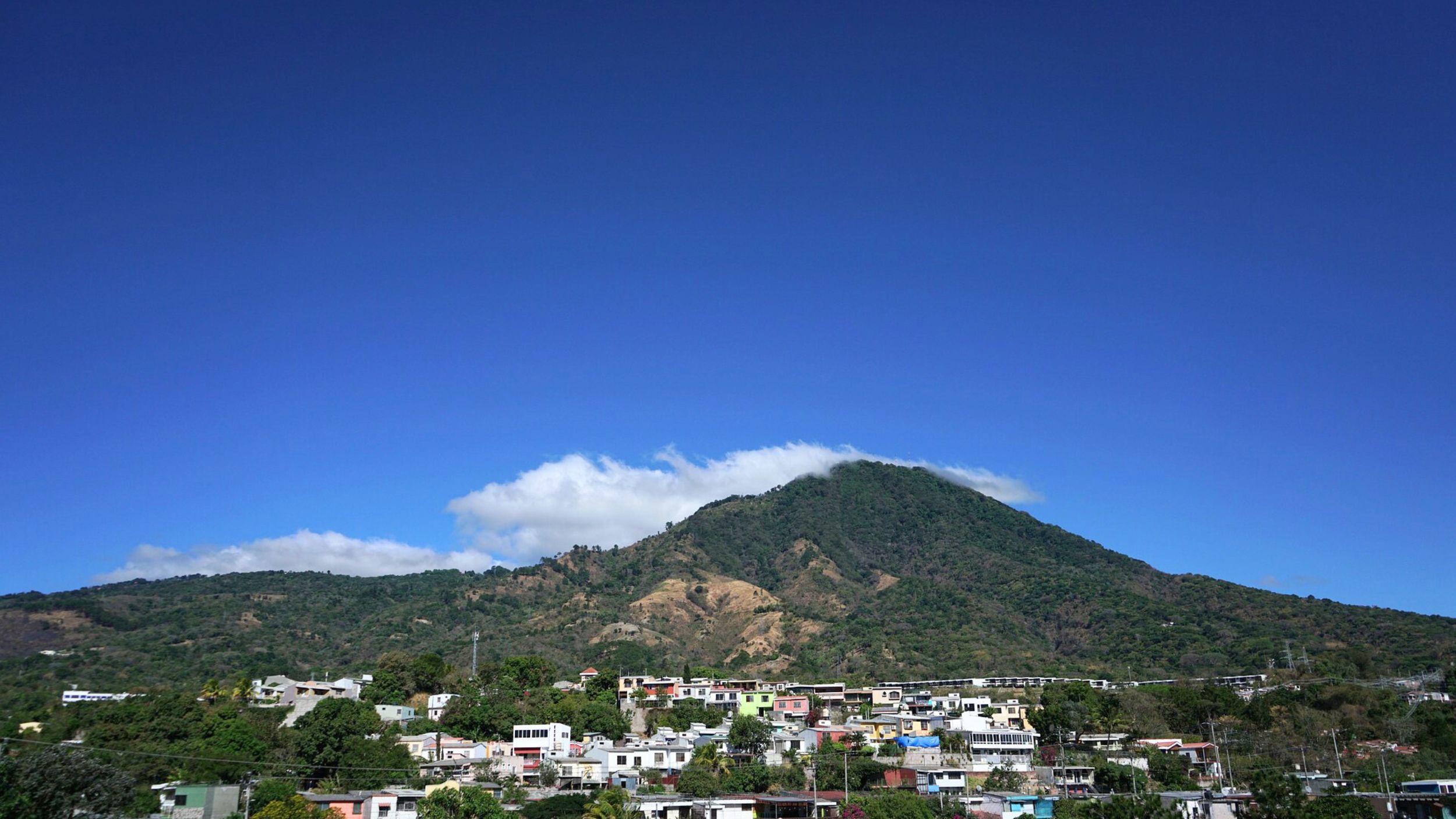 A landscape with housing and a mountain against a blue sky with some clouds
