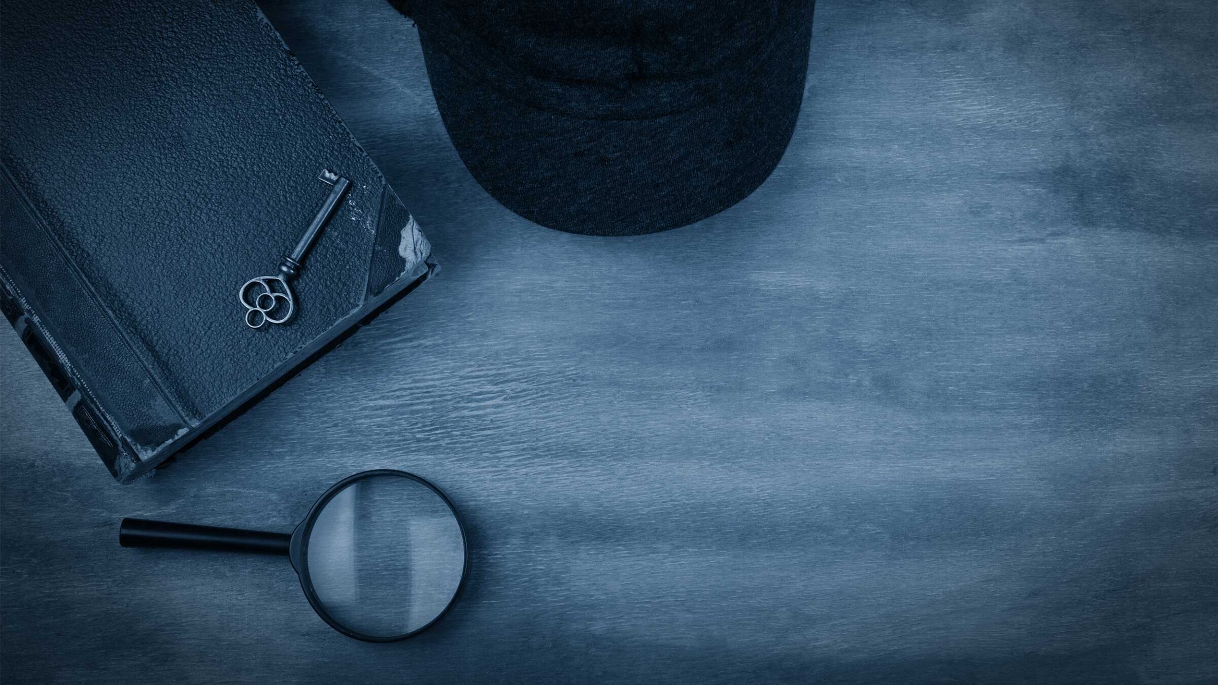 black and white image of a notebook, key, hat, and magnifying glass