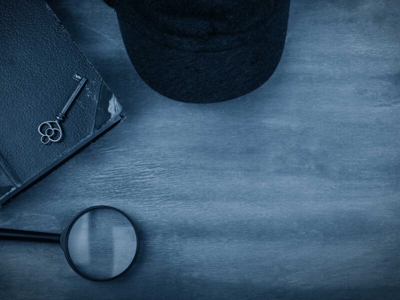 black and white image of a notebook, key, hat, and magnifying glass