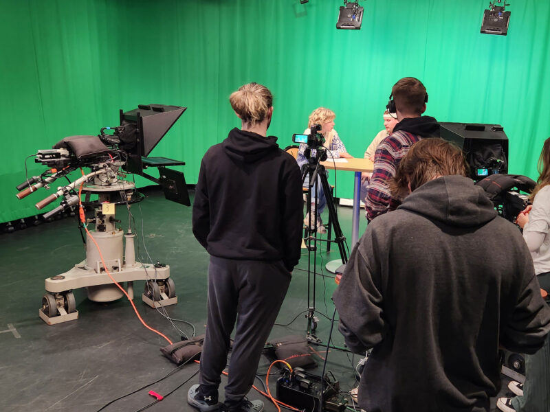 a group of students broadcasting in front of a green screen at Champlain's film stage with cameras and mics